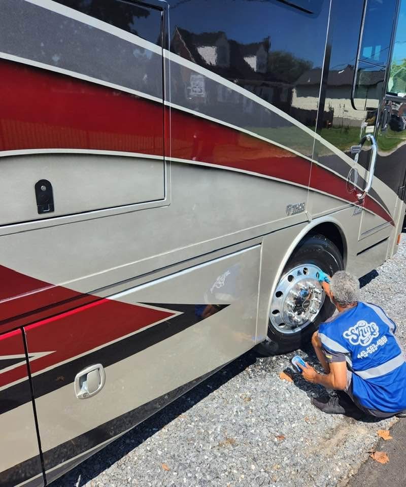 A Class A motorhome being detailed by Pinnacle, with a detailer working on the chrome wheel