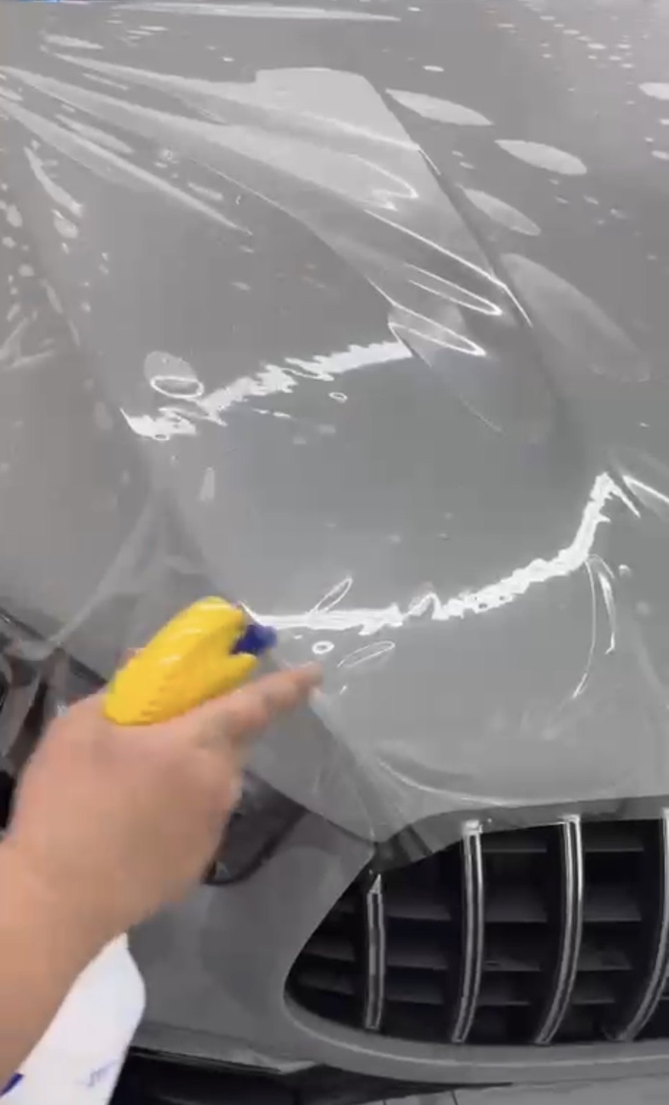 Slip solution being sprayed over paint protection film on the front of a car before it is worked down