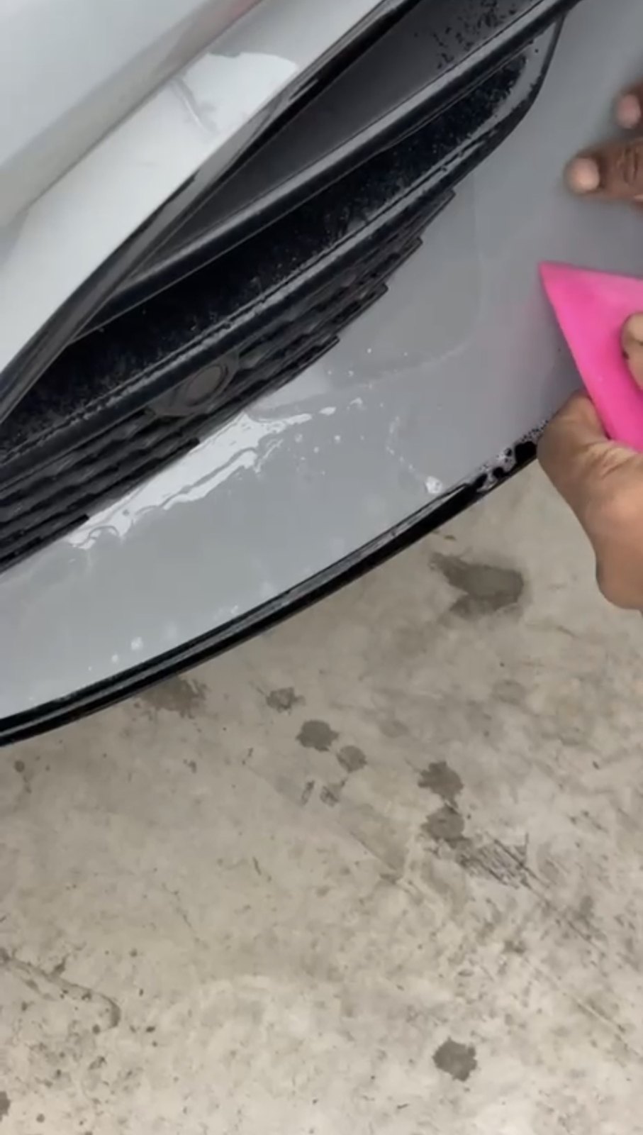 Paint protection film being squeegeed down along the edge of a front bumper