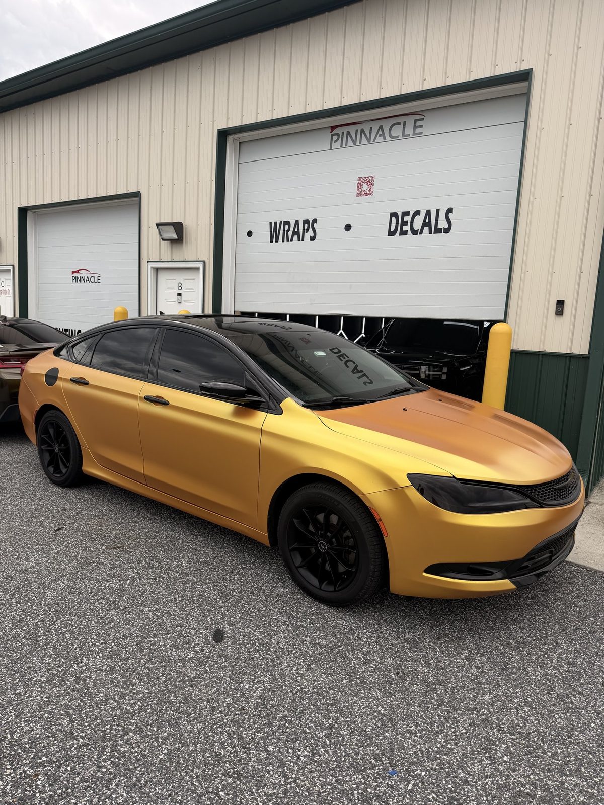 Sedan finished in a gold satin wrap with a gloss black roof, parked outside the Pinnacle shop bay